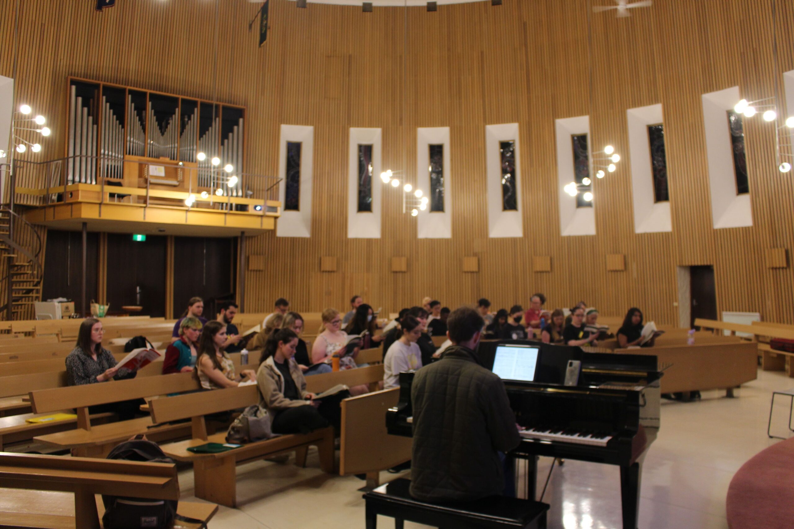 A typical rehearsal in the Religious Centre. We see our pianist Zac playing, and rows of choristers looking at their music and singing.