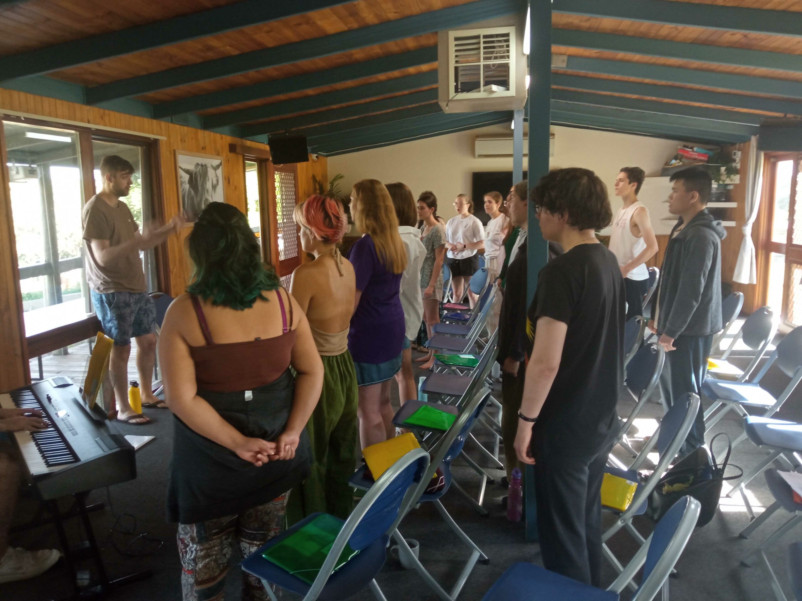 A rehearsal in progress - mostly we see the backs of rows of choristers standing up, watching our conductor at the left of the room