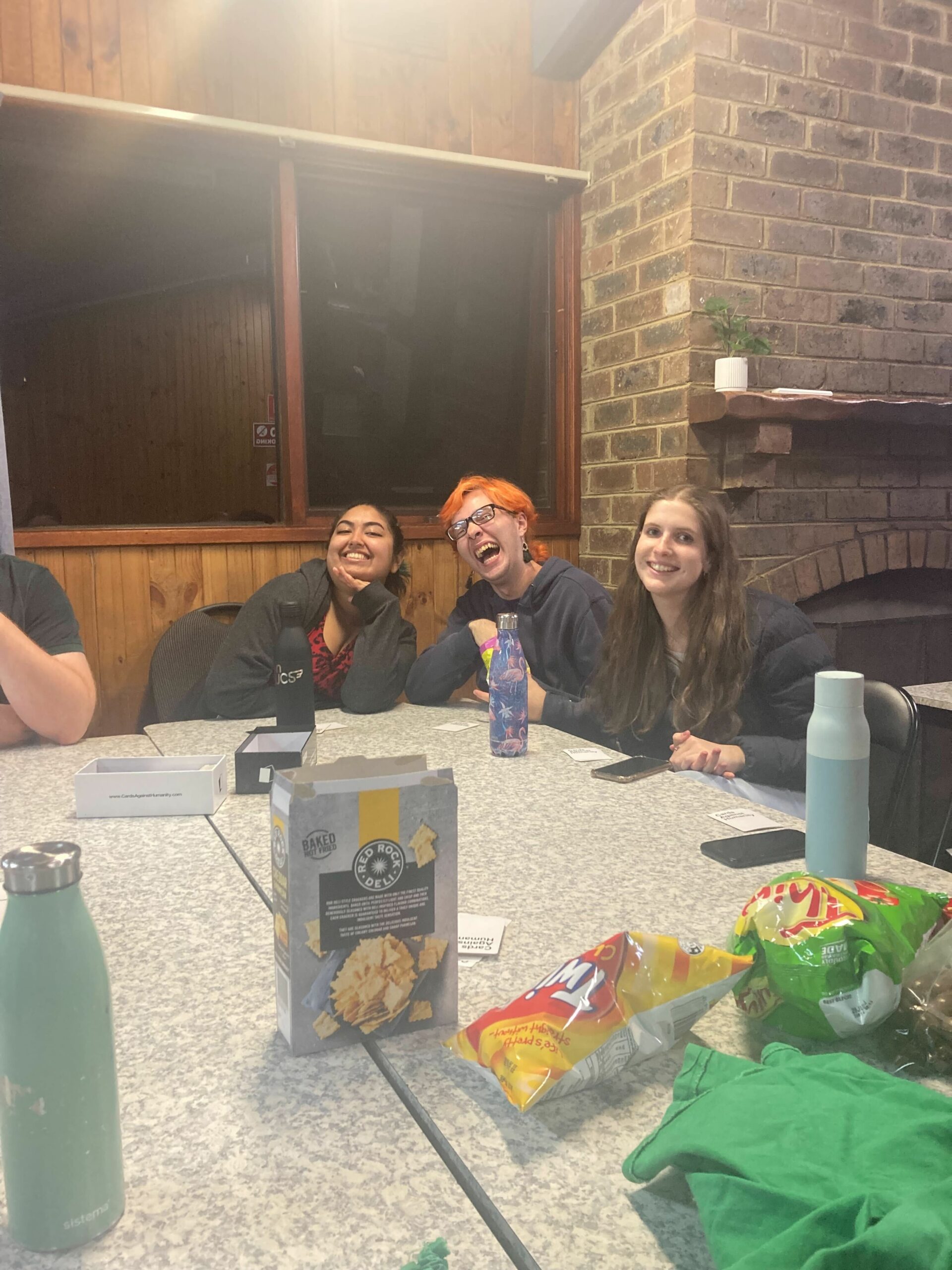 At the other end of a big table with lots of snacks and drinkbottles on it, three members of our committee strike jovial poses and look towards the camera