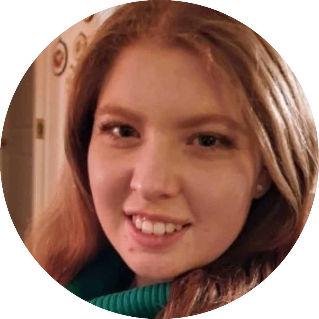 Maddie smiles at a slight angle into the camera. She has light brown hair and a small amount of a dark green top she is wearing is visible