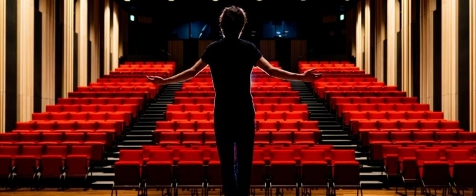 A silhoutted figure standing with arms outstretched in front of an empty theatre of seats.